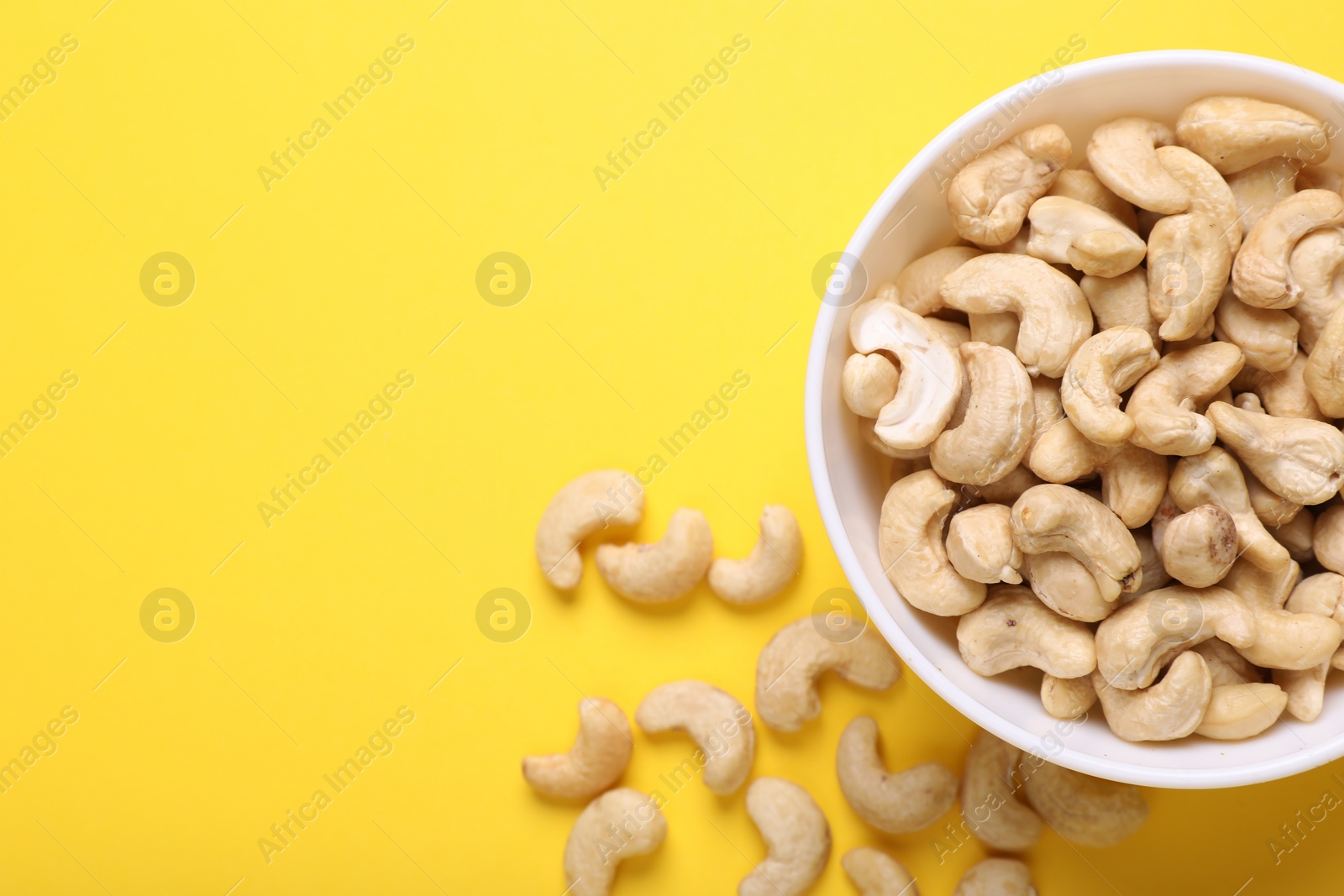 Photo of Tasty cashew nuts on yellow background, top view. Space for text