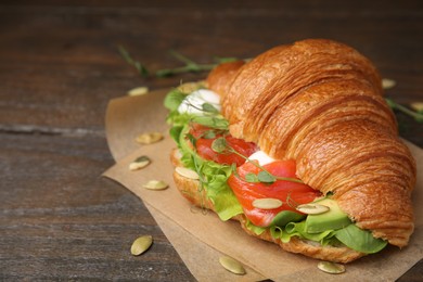 Photo of Tasty croissant with salmon, avocado, mozzarella and lettuce on wooden table, closeup. Space for text