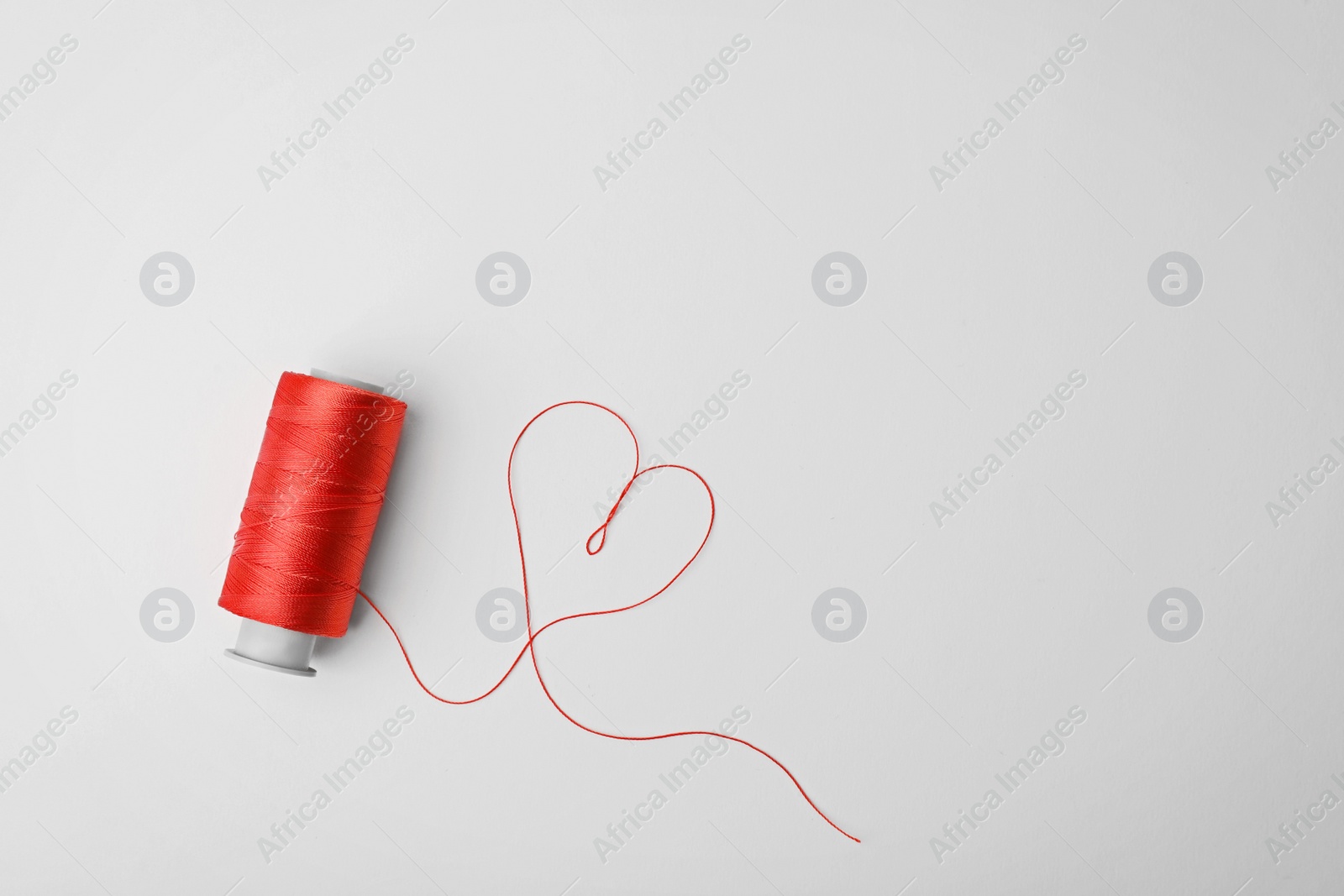 Photo of Heart made of color sewing thread and spool on white background, top view