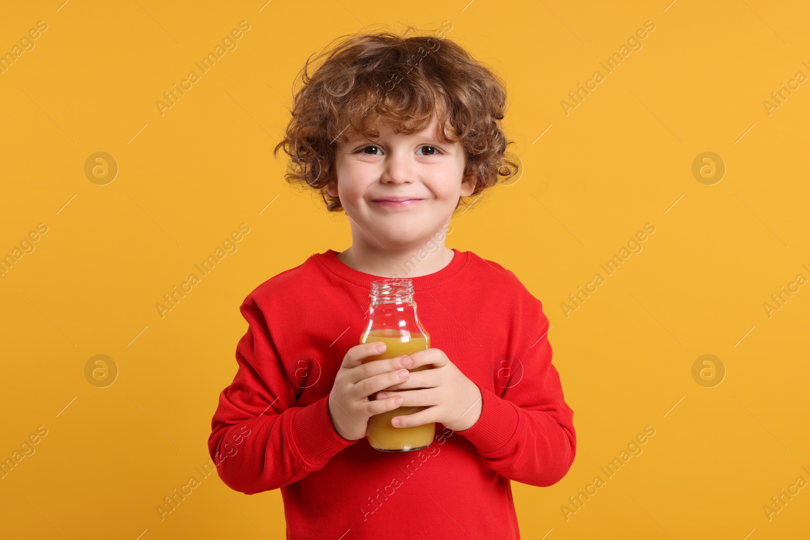 Photo of Cute little boy with glass bottle of fresh juice on orange background