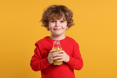 Photo of Cute little boy with glass bottle of fresh juice on orange background