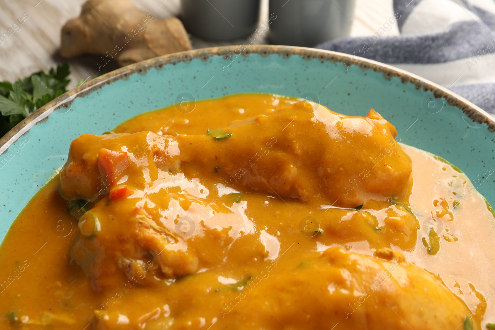 Photo of Tasty chicken curry, parsley and ginger on wooden table, closeup