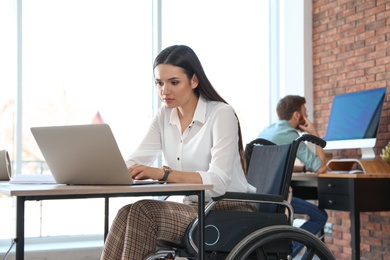 Photo of Young woman in wheelchair using laptop at workplace