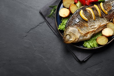 Photo of Tasty homemade roasted crucian carp with garnish on black table, top view and space for text. River fish