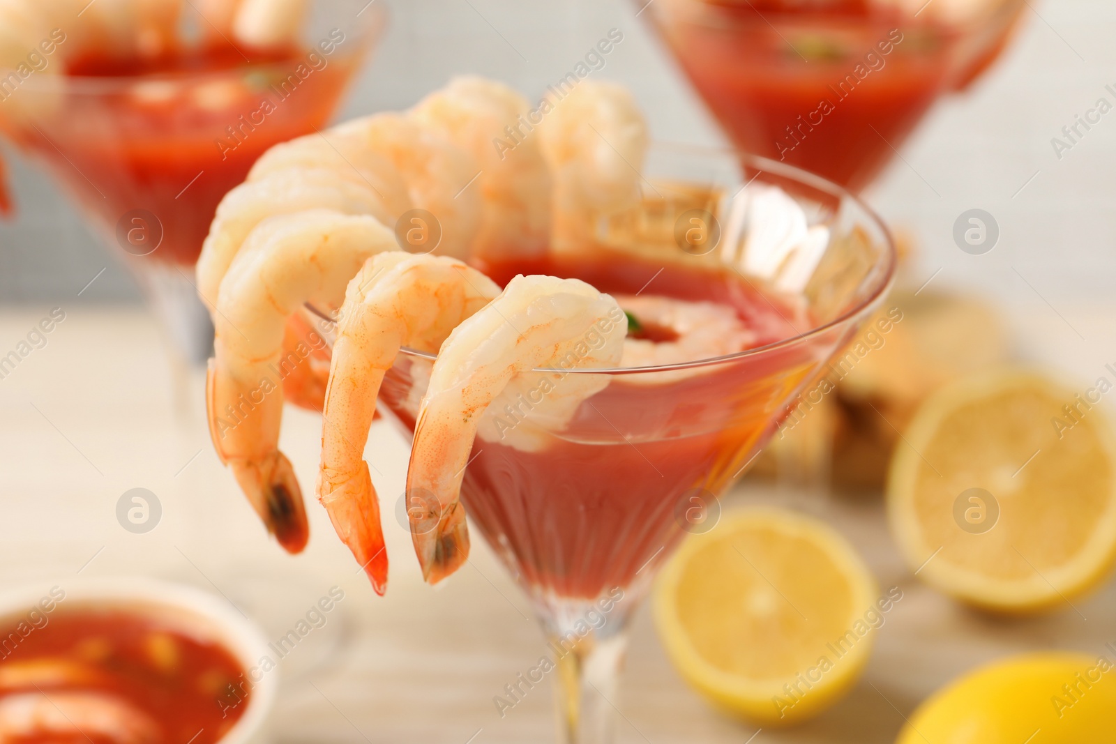 Photo of Tasty shrimp cocktail with sauce in glasses and lemon on table, closeup