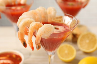 Tasty shrimp cocktail with sauce in glasses and lemon on table, closeup