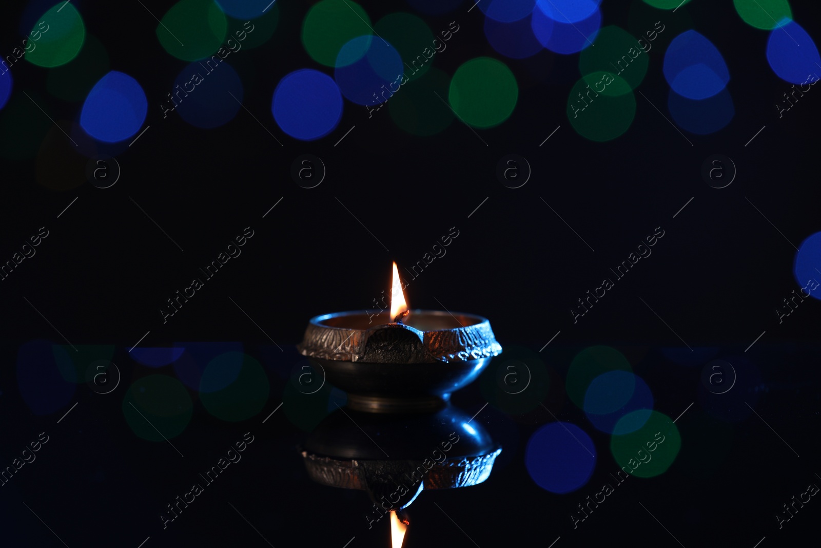 Photo of Lit diya on dark background with blurred lights, space for text. Diwali lamp