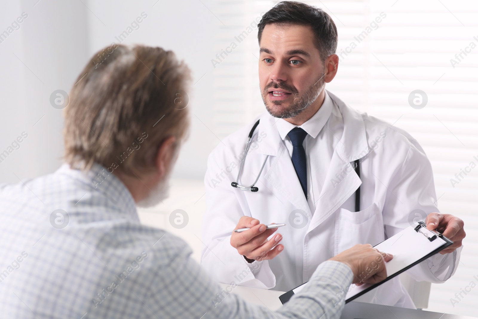 Photo of Doctor consulting senior patient at table in clinic