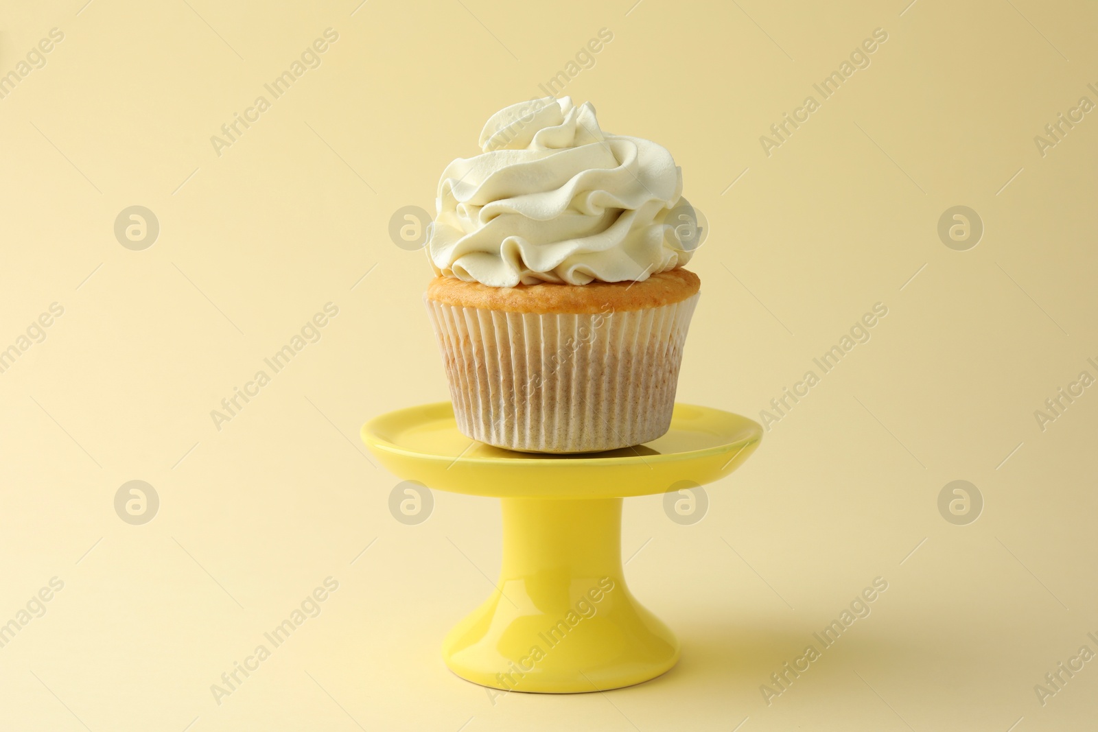 Photo of Tasty vanilla cupcake with cream on pale yellow background