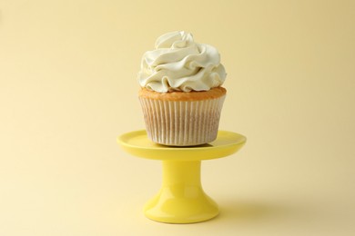 Photo of Tasty vanilla cupcake with cream on pale yellow background