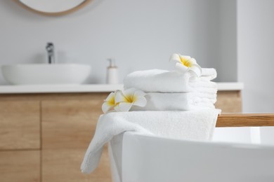 Photo of Fresh white towels and plumeria flowers on tub in bathroom. Space for text