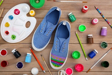 Photo of Light blue sneakers and painting supplies on wooden table, flat lay. Customized shoes