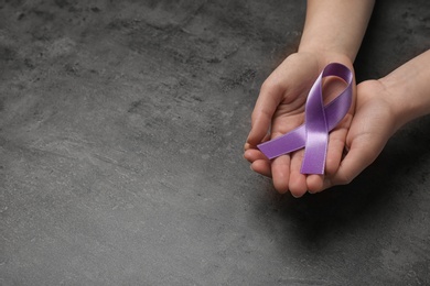 Woman holding purple awareness ribbon on grey background, space for text