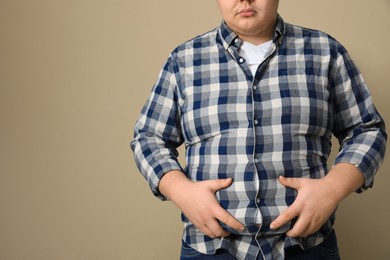 Overweight man in tight shirt on beige background, closeup. Space for text