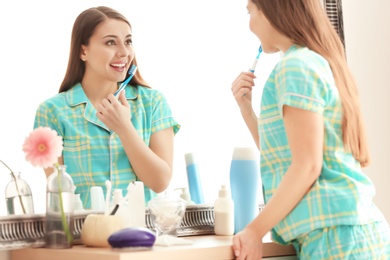 Photo of Young woman looking in mirror while brushing teeth indoors