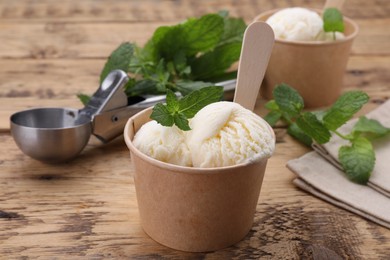Paper cups with delicious ice cream and mint on wooden table, closeup