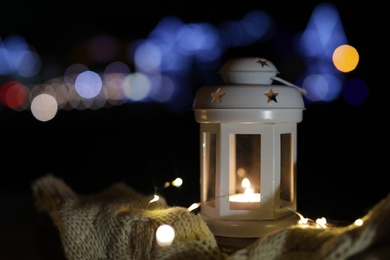 Photo of Lantern, sweater and Christmas lights outdoors on winter night. Space for text