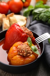 Photo of Delicious stuffed peppers with basil in bowl on wooden table, closeup