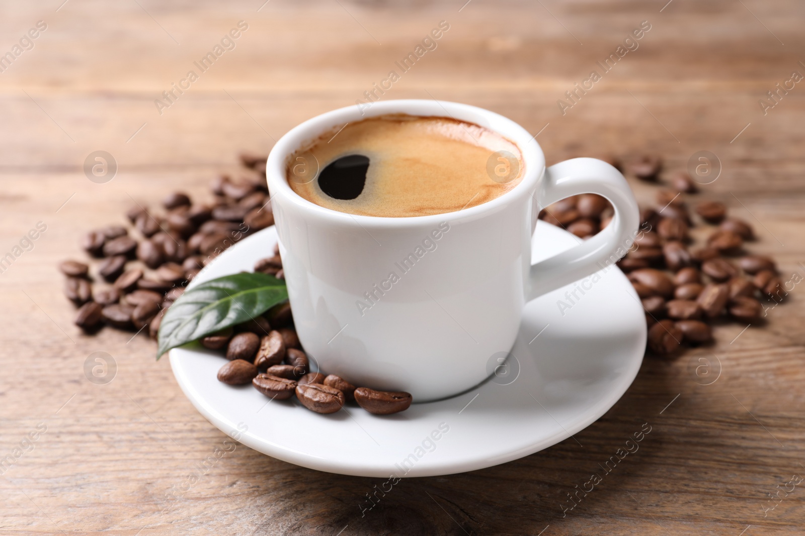 Photo of Cup of hot aromatic coffee and roasted beans on wooden table