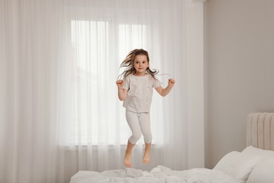 Photo of Cute little girl jumping on bed at home