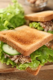 Photo of Delicious sandwiches with tuna, cucumber and lettuce leaves on wooden board, closeup