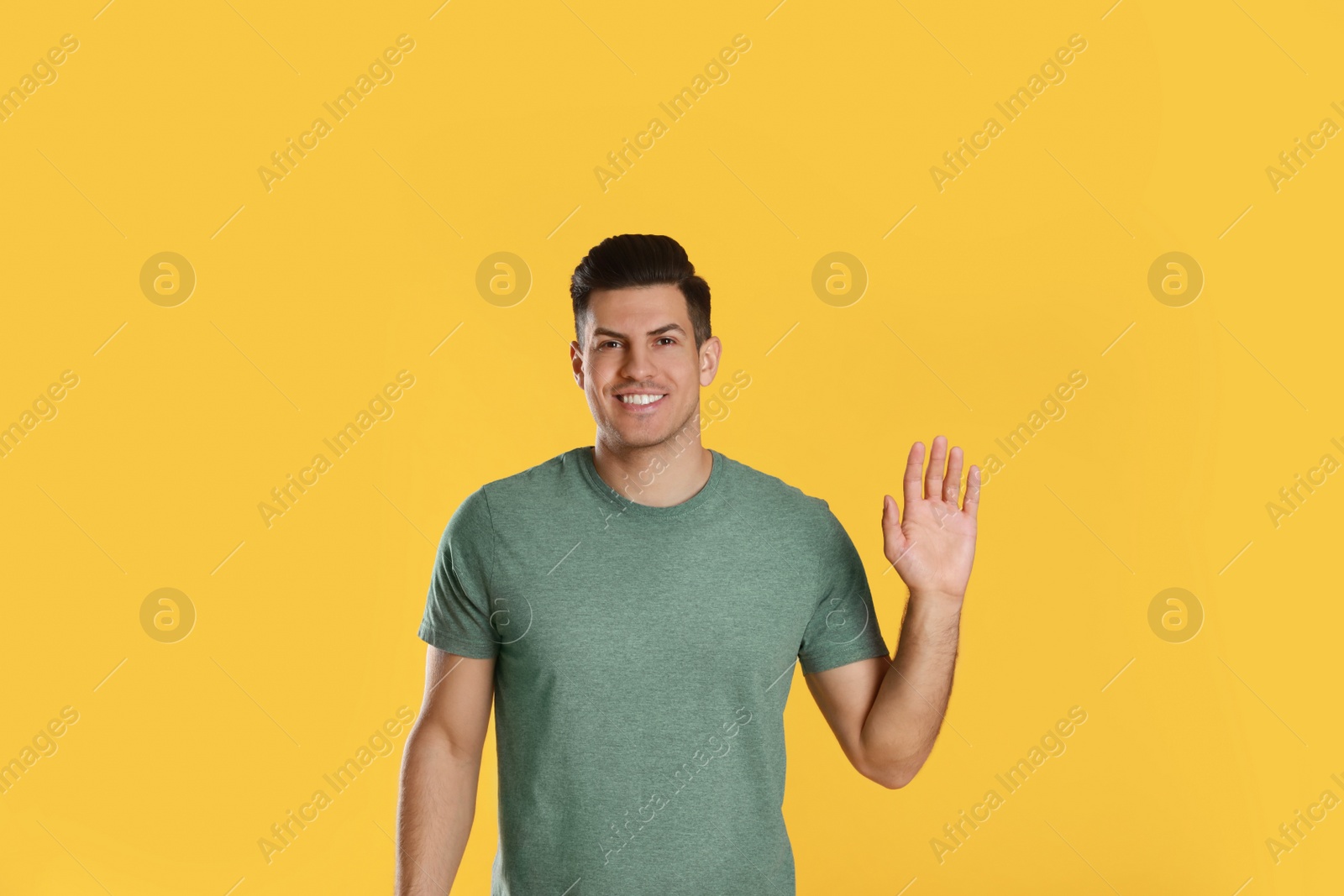 Photo of Cheerful man waving to say hello on yellow  background