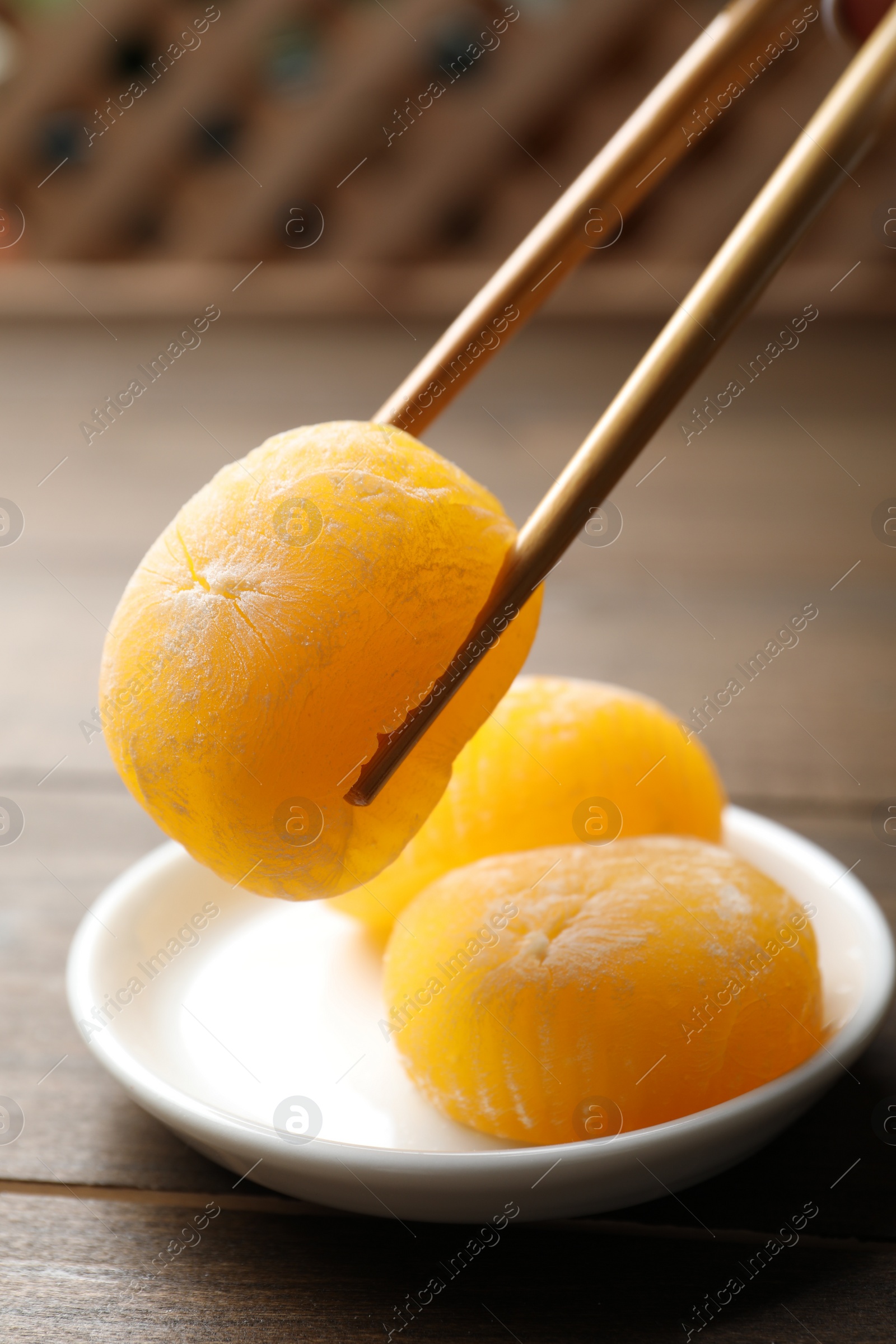 Photo of Taking delicious mochi from plate with chopsticks on wooden table. Traditional Japanese dessert