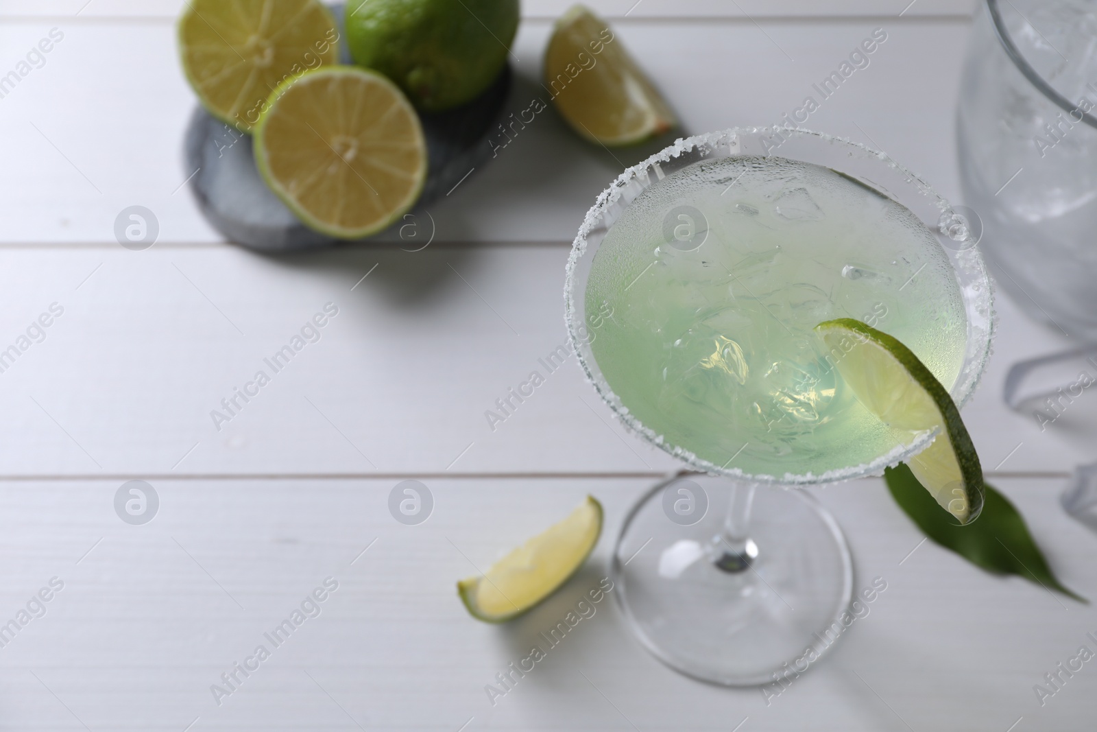 Photo of Delicious Margarita cocktail in glass and limes on white wooden table, above view. Space for text