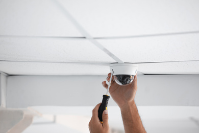 Technician installing CCTV camera on ceiling indoors, closeup