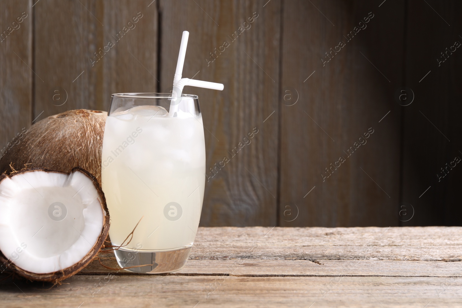 Photo of Glass of coconut water, ice cubes and nuts on wooden table, space for text