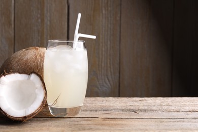 Photo of Glass of coconut water, ice cubes and nuts on wooden table, space for text