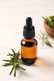 Bottle with essential oil and fresh rosemary on white wooden table