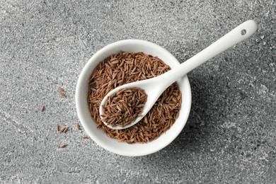 Photo of Bowl of caraway (Persian cumin) seeds and spoon on gray textured table, top view