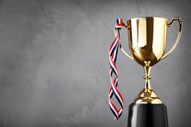 Photo of Golden trophy cup with ribbon on grey background. Space for text