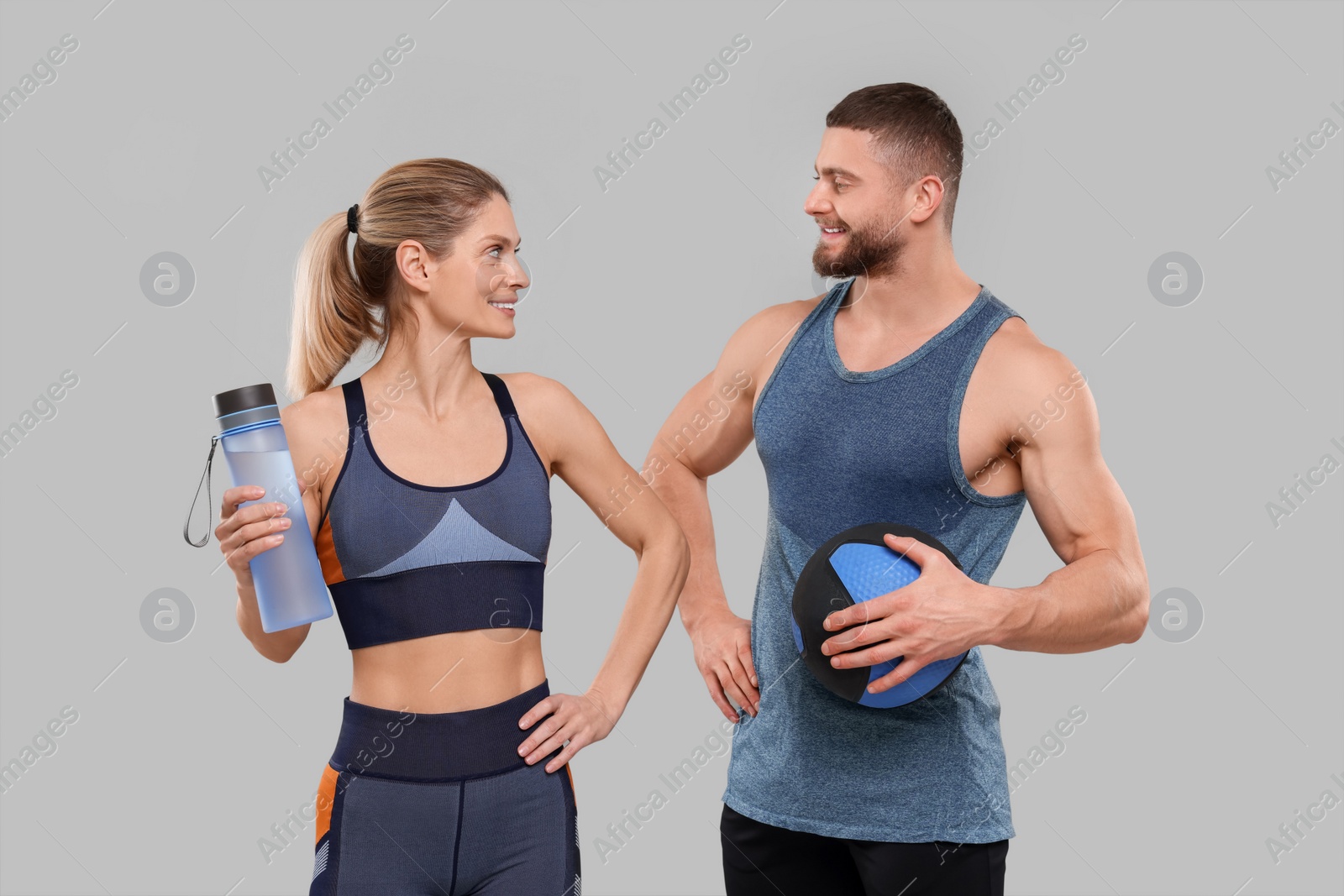 Photo of Athletic people with bottle of water and medicine ball on grey background