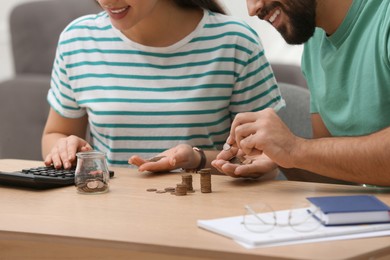 Happy young couple counting money at wooden table indoors, closeup