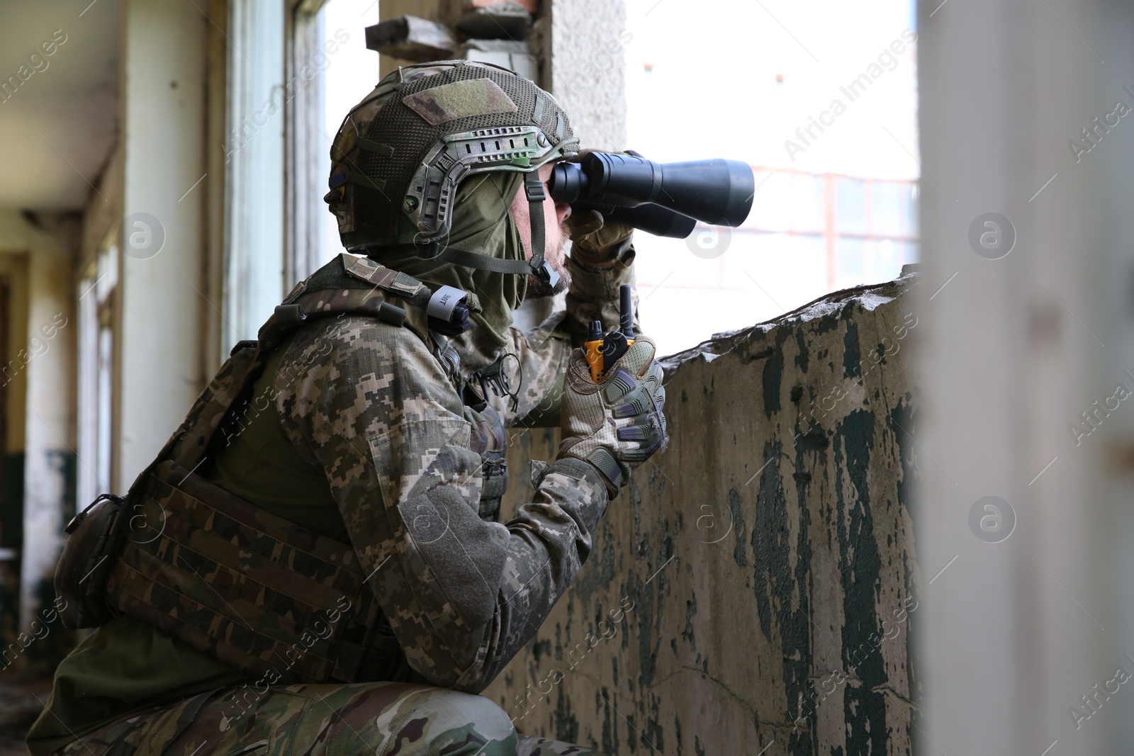 Photo of Military mission. Soldier in uniform with binoculars inside abandoned building