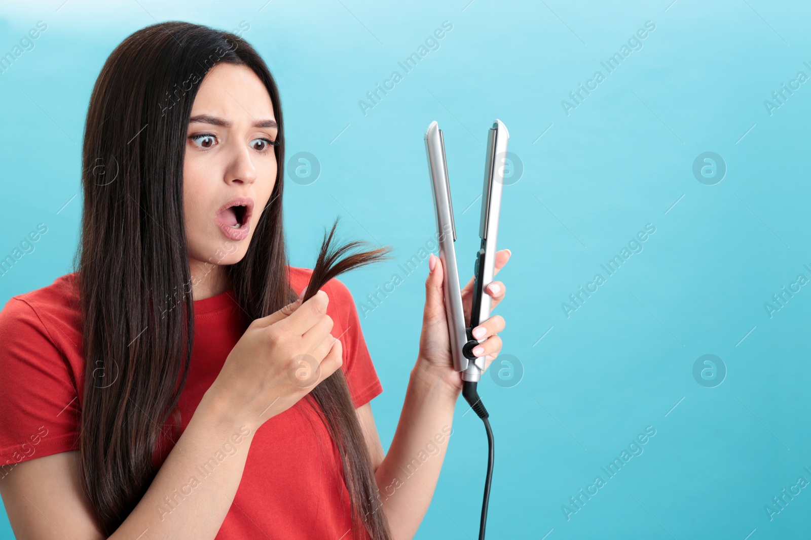 Photo of Upset woman with hair iron on blue background, space for text