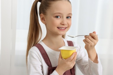 Cute little girl with tasty yogurt indoors