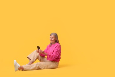 Photo of Senior woman with phone on orange background, space for text