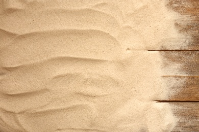 Beach sand on wooden background, top view with space for text