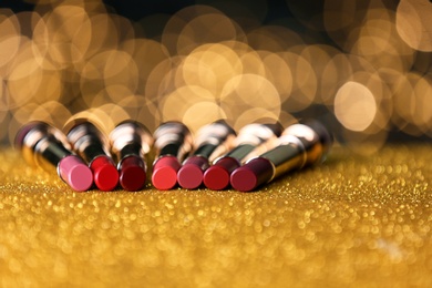 Photo of Set of bright lipsticks on table with gold glitter against blurred lights, space for text