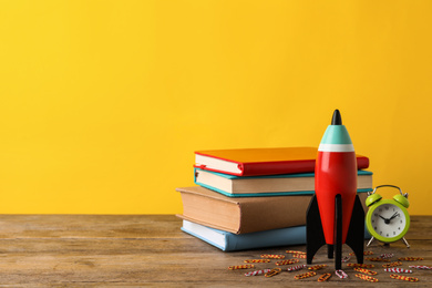 Bright toy rocket and school supplies on wooden desk. Space for text