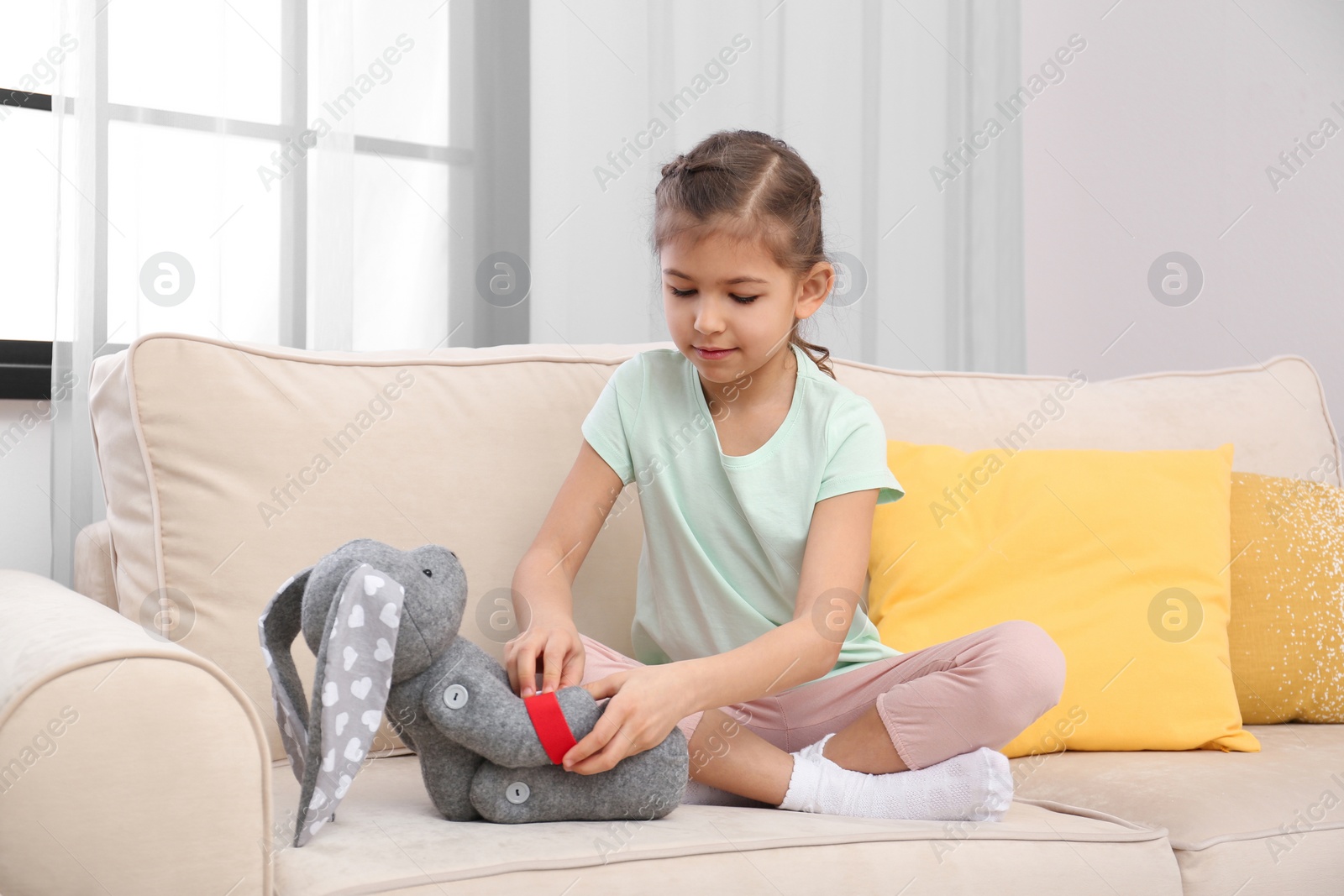 Photo of Cute child playing doctor with stuffed toy on sofa in hospital