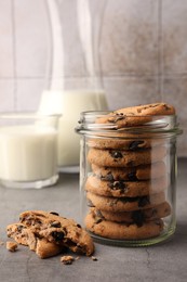 Photo of Glass jar with delicious chocolate chip cookies and milk on grey table