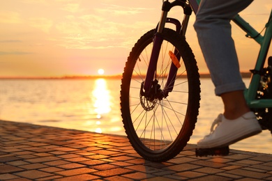 Photo of Woman riding bicycle on embankment at sunset, closeup