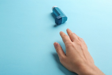 Woman reaching for asthma inhaler on color background, closeup. Space for text