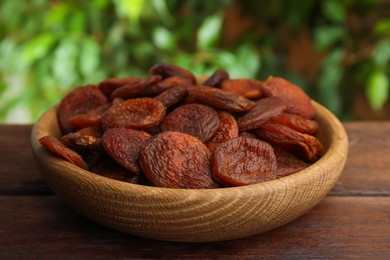 Photo of Bowl of tasty apricots on wooden table against blurred green background. Dried fruits
