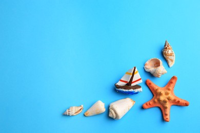 Photo of Beautiful starfish, decorative ship and shells on blue background, flat lay. Space for text