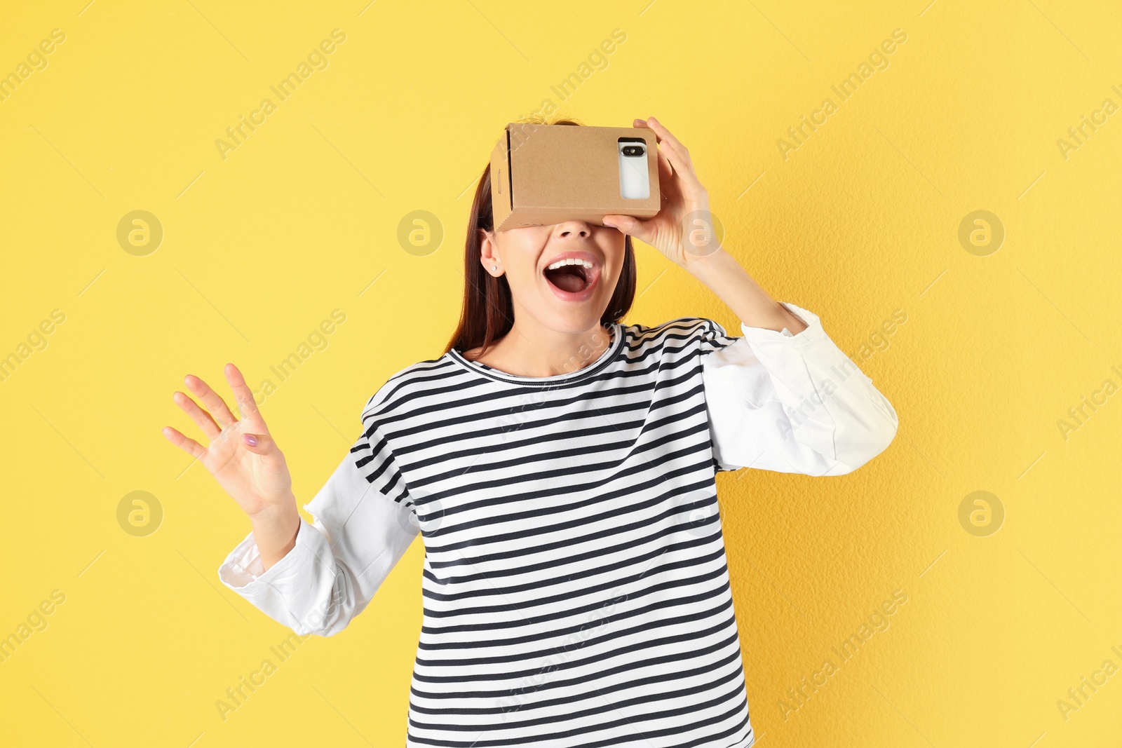 Photo of Young woman using cardboard virtual reality headset on color background